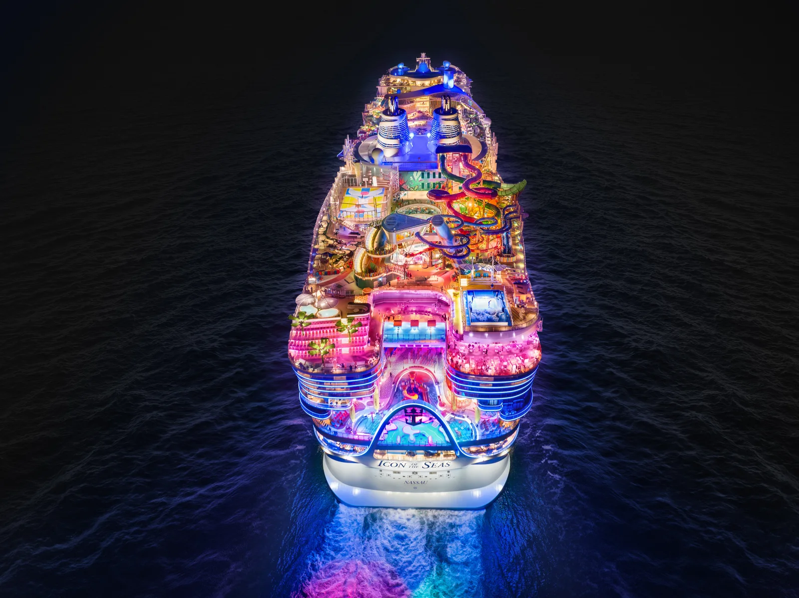 Icon of the Seas illuminated at night from directly above, all neighborhoods and pools lit across the full ship